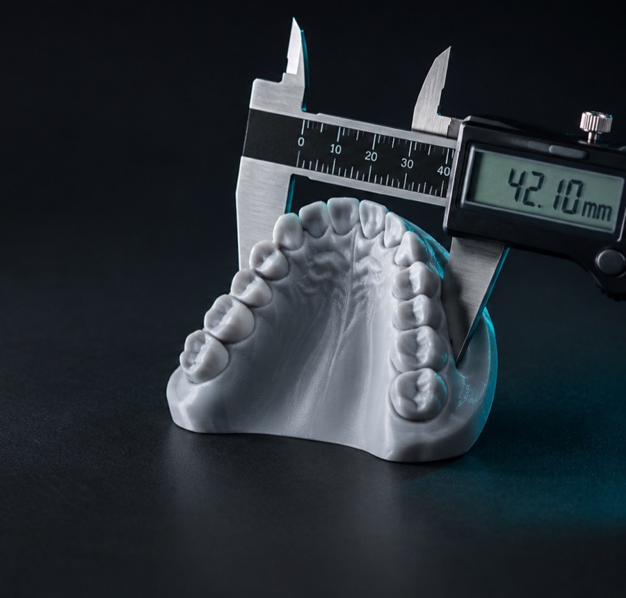 Modelo de arcada impresso em PLA cinza sendo medido com paquímetro digital marcando 42,10 mm